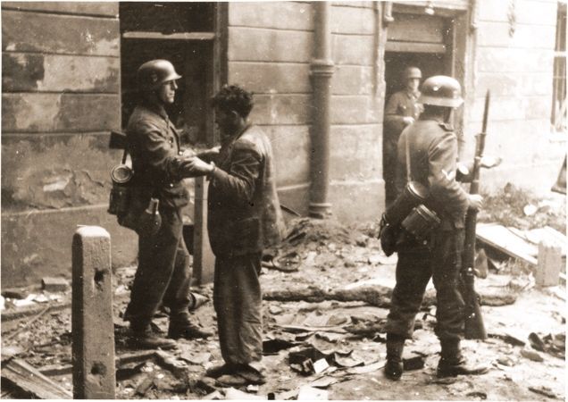 An SS soldier searches a captured Jewish resistance fighter during the suppression of the Warsaw ghetto uprising